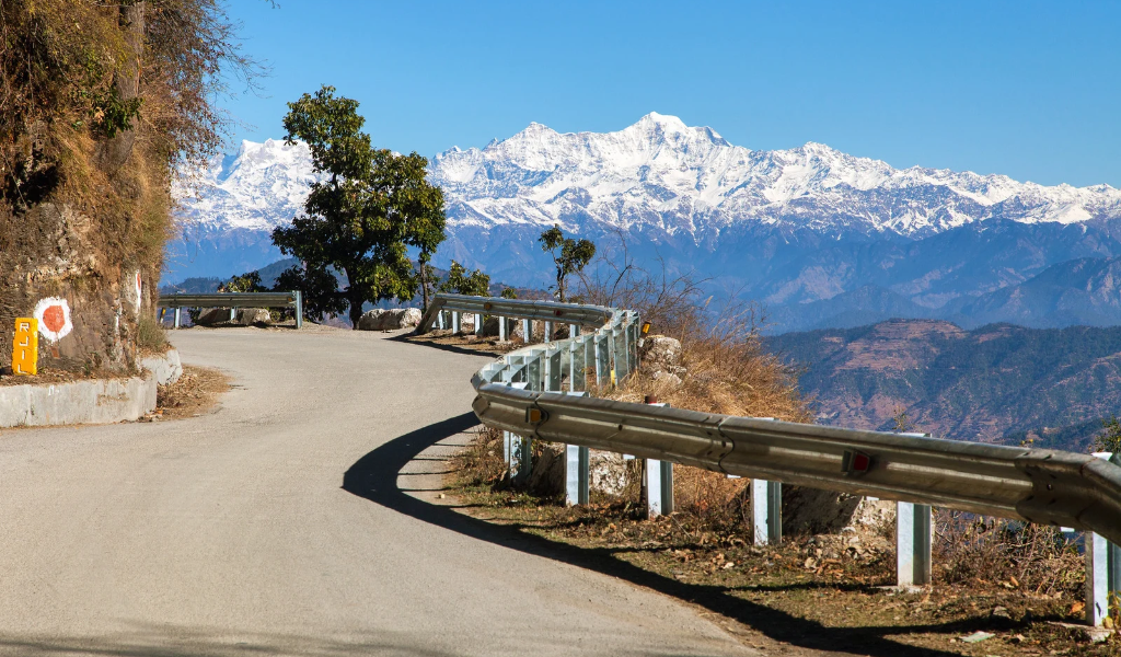 Scenic mountain road and snow-capped Himalayan peaks featured in our Kanatal tour package