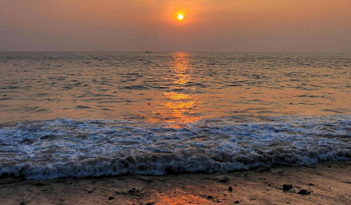 The sun setting over the Arabian Sea with golden reflections on the waves and a small boat on the horizon, highlighting the beauty of beach holidays in goa
