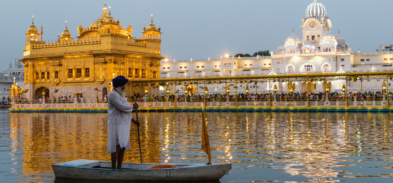 Golden Temple Amritsar Tour Package with Sikh man standing on boat in sarovar during evening