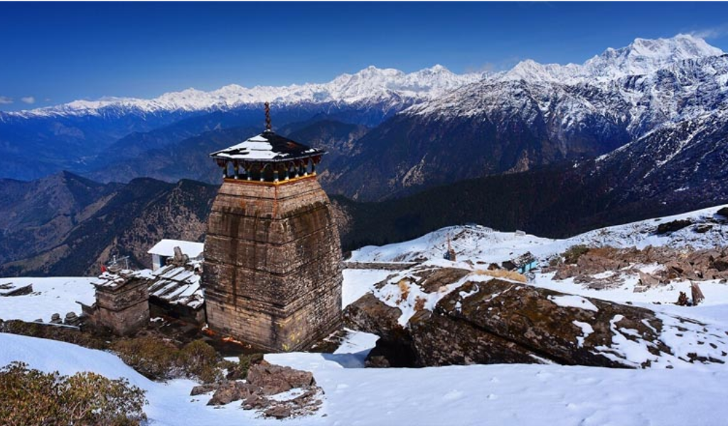 Binsar tour package ex Kathgodam showing snow-covered ancient Shiva temple with panoramic Himalayan peak background.