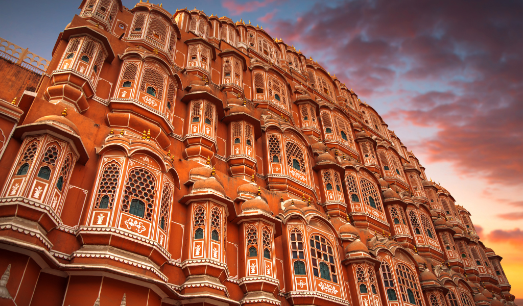 The detailed pink-orange facade of Hawa Mahal  in Jaipur against a cloudy sunset sky, showing the unique Rajput architecture Capture During Golden Triangle With Goa Tour package By Visitors.