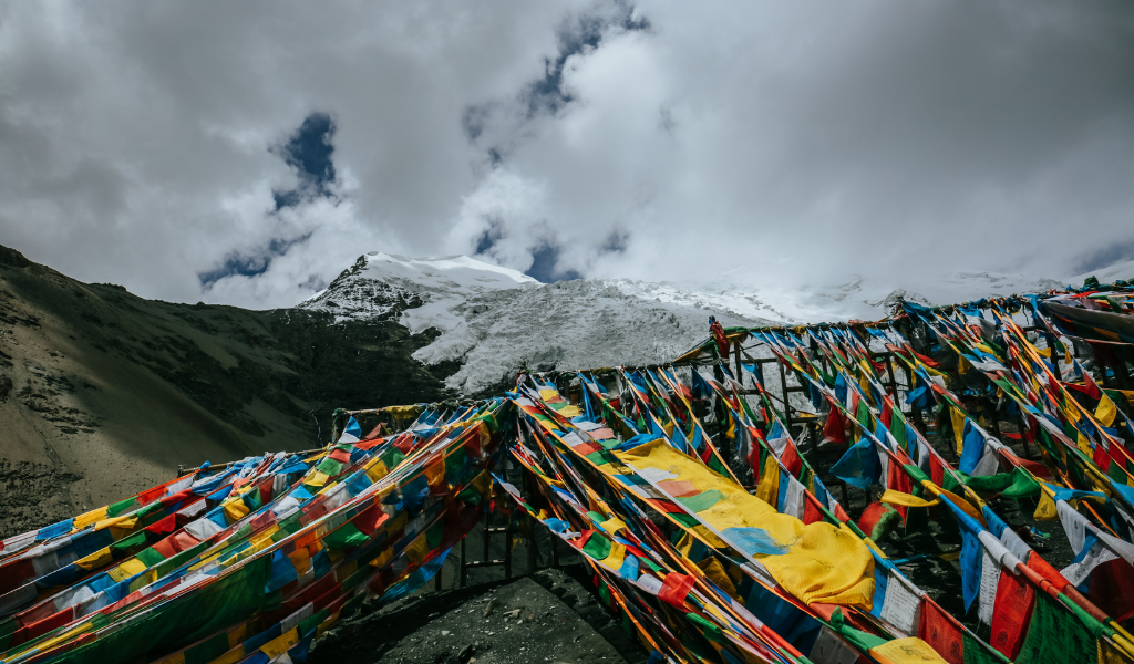 Colorful Buddhist prayer flags fluttering in the wind with the snow-covered peaks of the Vyas Valley in the background during the Adi Kailash and Om Parvat Tour package.