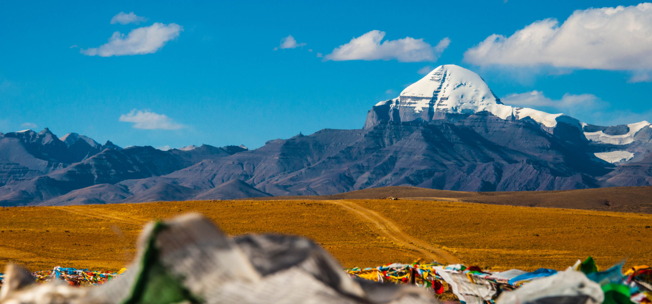 A wide-angle view of the snow-capped peak during the Adi Kailash and Om Parvat Yatra with prayer flags in the foreground.