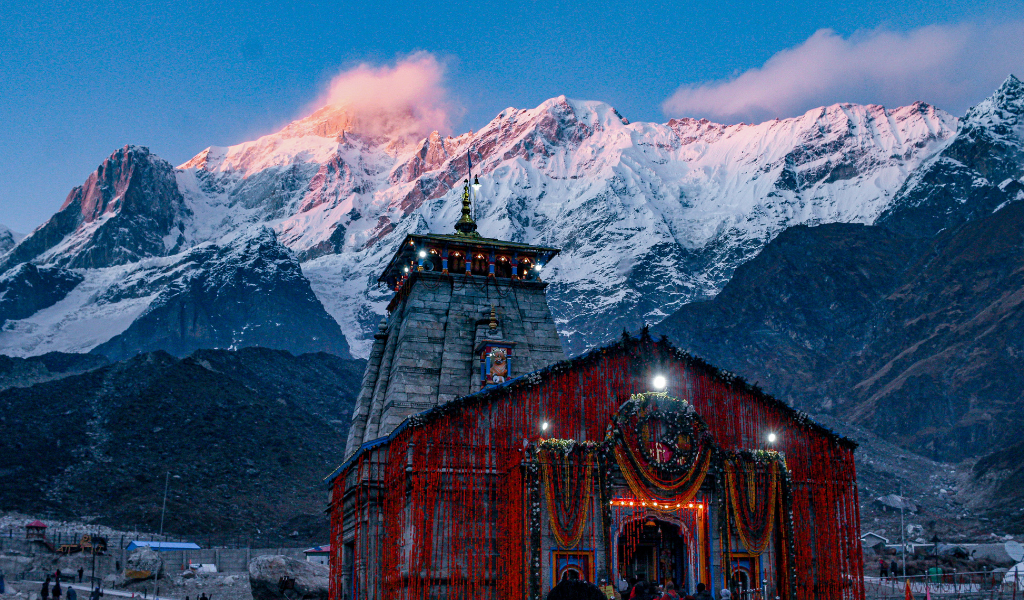 Chardham Yatra package view of Kedarnath temple illuminated at sunset with snow-clad Himalayan mountain peaks.