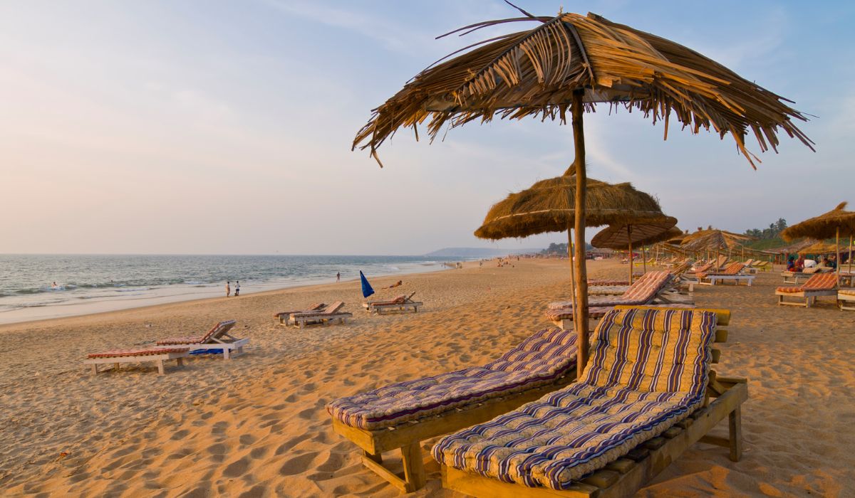 Relaxing wooden sun loungers under straw umbrellas on a sandy beach during sunset, highlighting a Perfect Couple luxury Goa vacation.