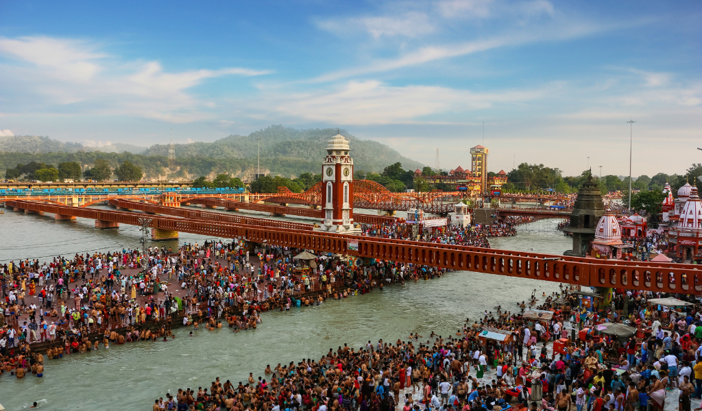 A wide view of the crowded Har Ki Pauri ghat and clock tower in Haridwar, a major stop in our Ayodhya Varanasi Haridwar Rishikesh tour package.