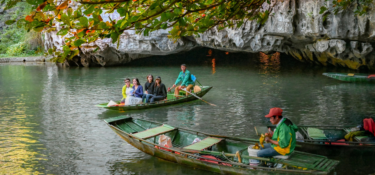 A group of tourists enjoying a scenic rowing boat ride near a limestone cave river during Vietnam trip package from Hanoi to Halong Bay.