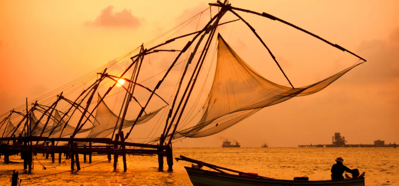 Chinese fishing nets at sunset in Kerala with a small boat on calm sea creating a golden scenic view