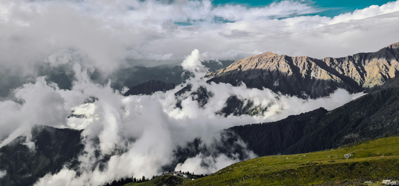 Beautiful mountain valley with low-floating clouds and green meadows on a chopta trek package.