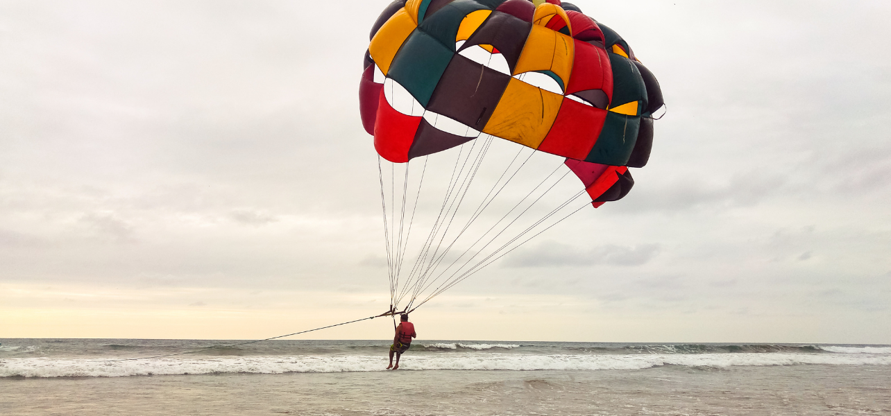 A traveler parasailing over the ocean with a colorful parachute during a 2nights 3 days Goa Holiday Trip, showcasing popular water sports available for tourists