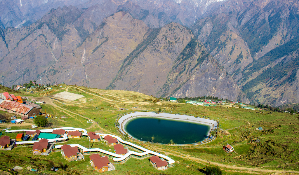 Auli artificial lake view surrounded by green meadows, mountain resorts, and Garhwal Himalayan peaks in Uttarakhand image captured During Auli chopta Tour Package.