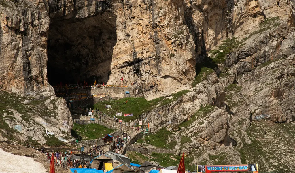 Yatri climbing the stairs toward the entrance of the Amarnath Holy Cave for Darshan, featuring the rugged mountain terrain and prayer flags.