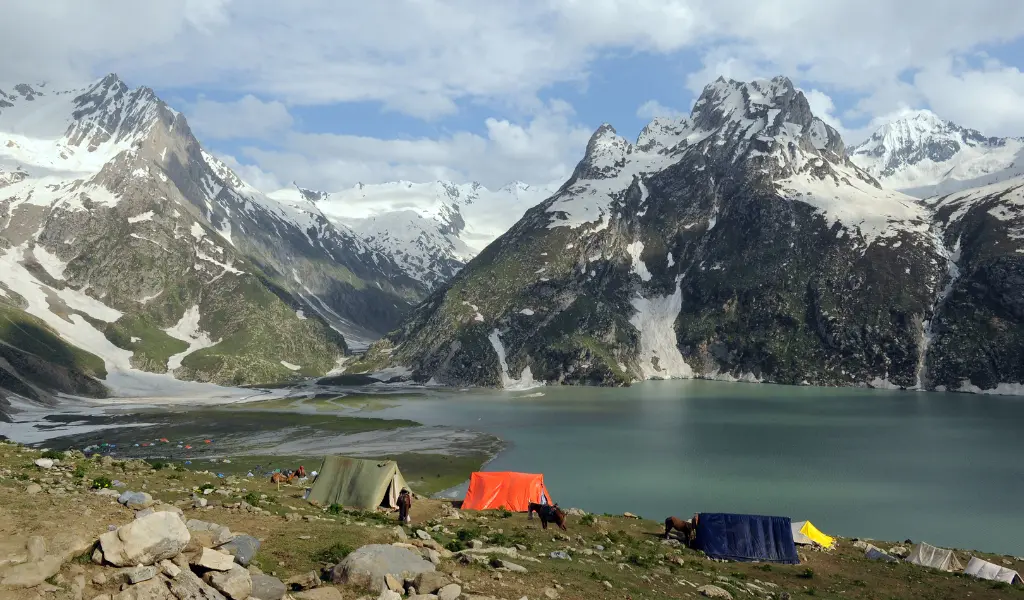 A high-altitude view of the turquoise Sheshnag Lake surrounded by snow-capped Himalayan peaks on the traditional Amarnath Yatra route.