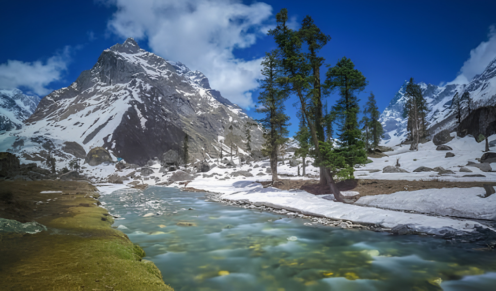 Glacial Supin river flowing through snow-covered trails and pine trees against towering Himalayan peaks on the Har Ki Dun trek.