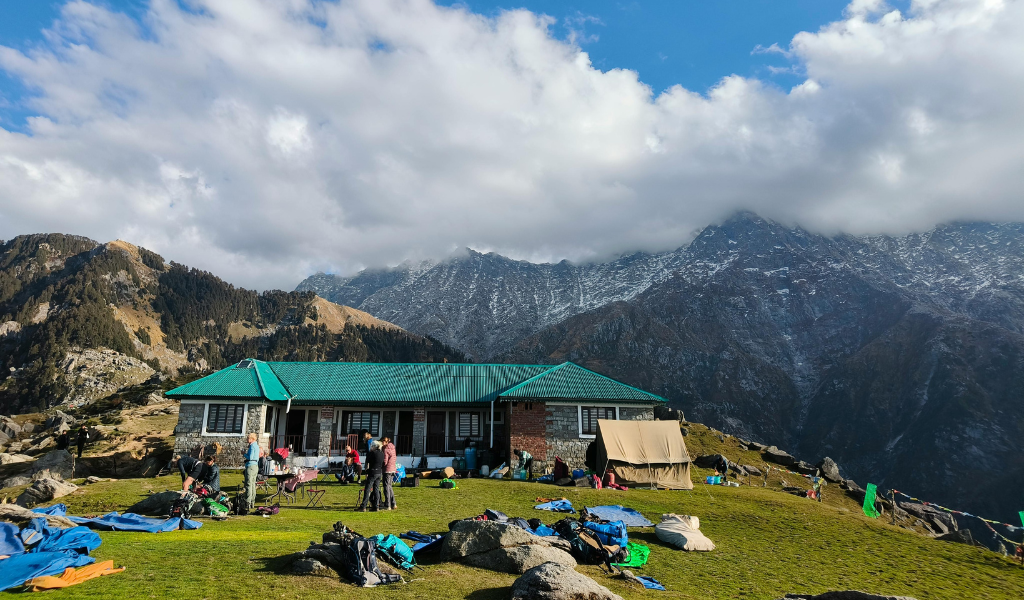 Tourists relaxing outside a mountain lodge with tents and Dhauladhar Himalayan range backdrop in Shimla trip package