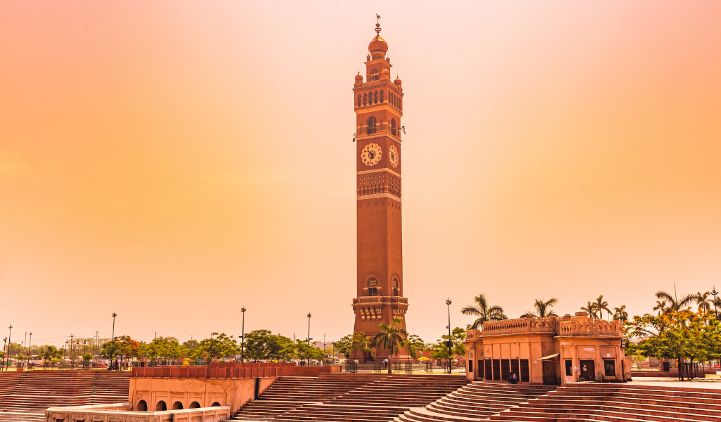 The tall Husainabad Clock Tower under an orange sky, a famous landmark to see during your Lucknow city tour and Lucknow tour package