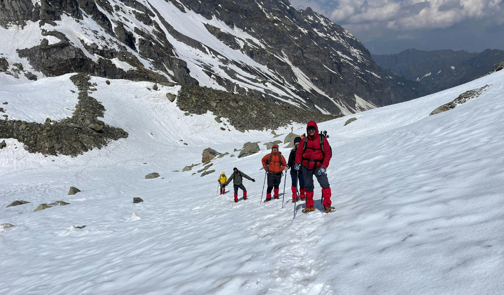 Group of trekkers in winter jackets and gaiters hiking through deep snow on the Kuari Pass trek route.